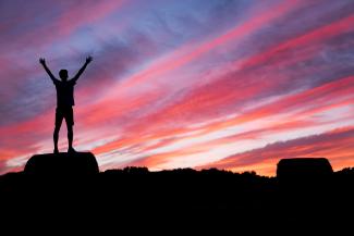 silhouette of man standing on high ground under red and blue skies by Benjamin Davies courtesy of Unsplash.